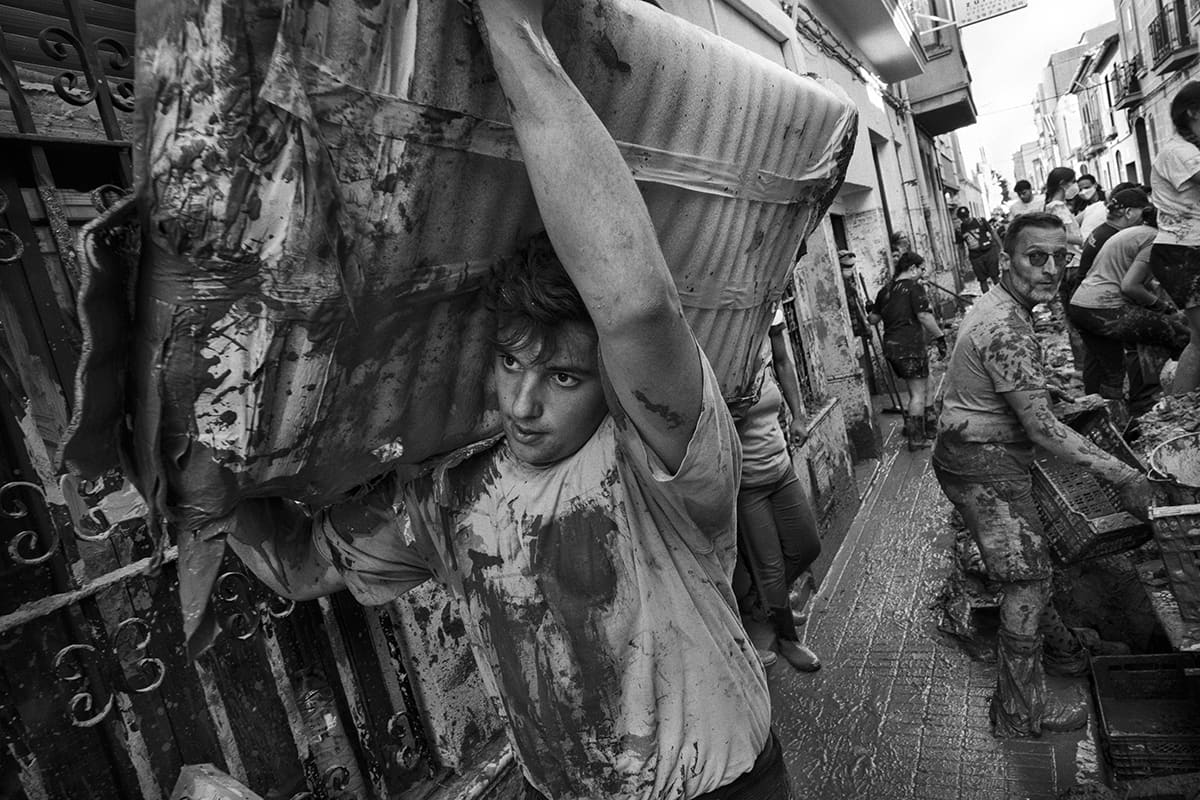 Volunteer carrying debris on his shoulder through the mud-covered streets of Paiporta after the DANA flood in Valencia