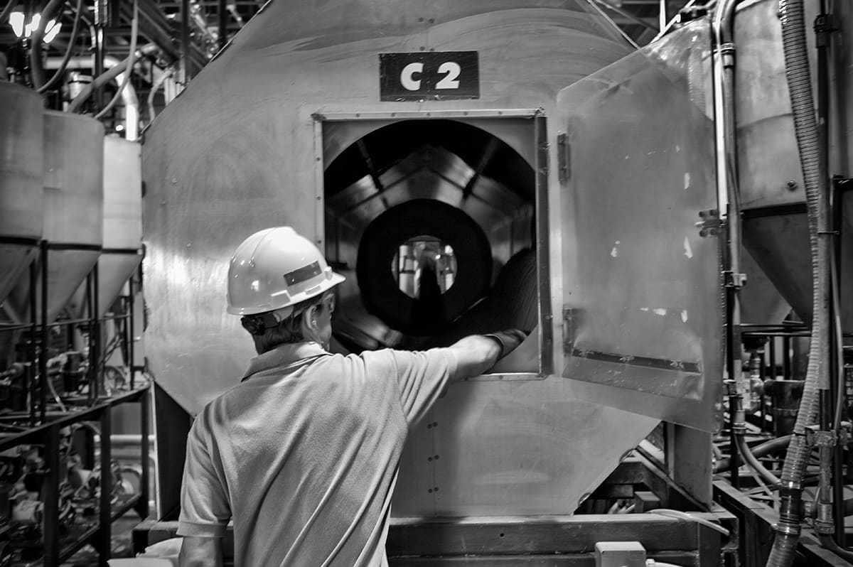 A worker in a hard hat inspects the open hatch of a large industrial machine marked C2.