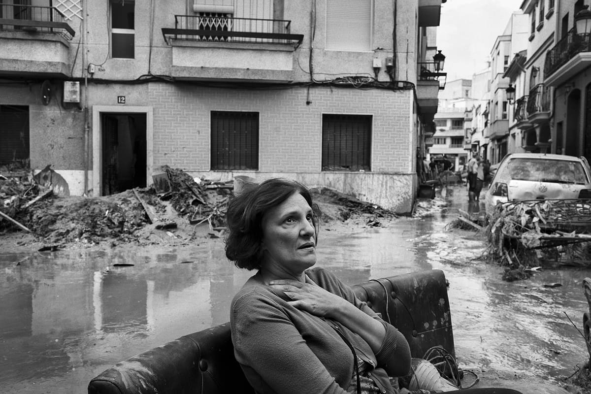 Woman sitting in the street watching the mud-covered remains of her home in Paiporta after the Valencia DANA