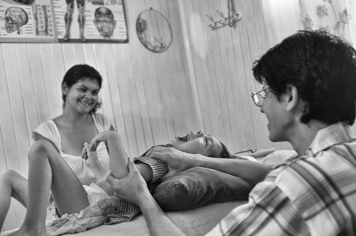 A man massages the leg of a child lying on a treatment table while a smiling woman holds the child.