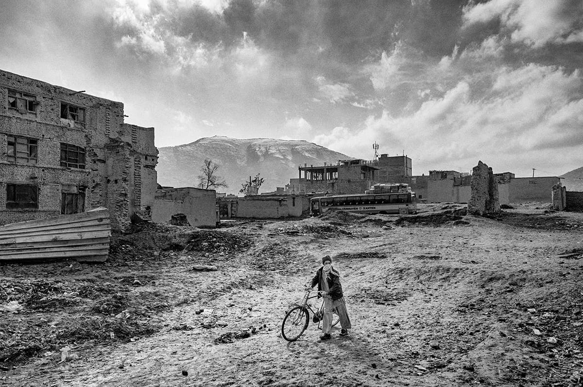 Young Afghan boy with a bicycle in front of war-damaged buildings in Kabul, February 2009