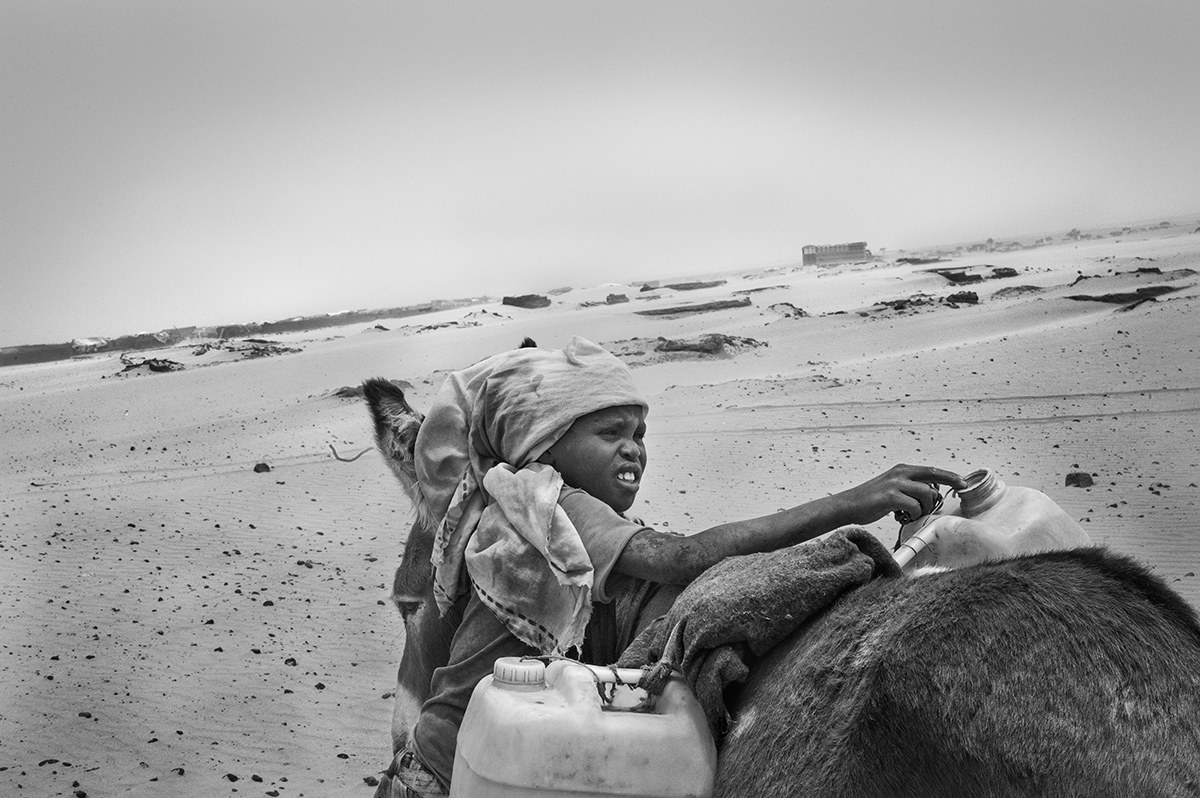 Boy loading water jerrycans onto a donkey in the desert outside a camp in Darfur, Sudan.