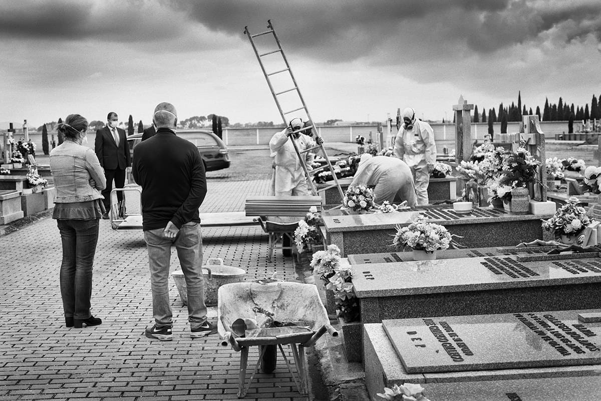 Burial of a COVID-19 victim in a Spanish cemetery with staff in protective suits and relatives keeping distance.
