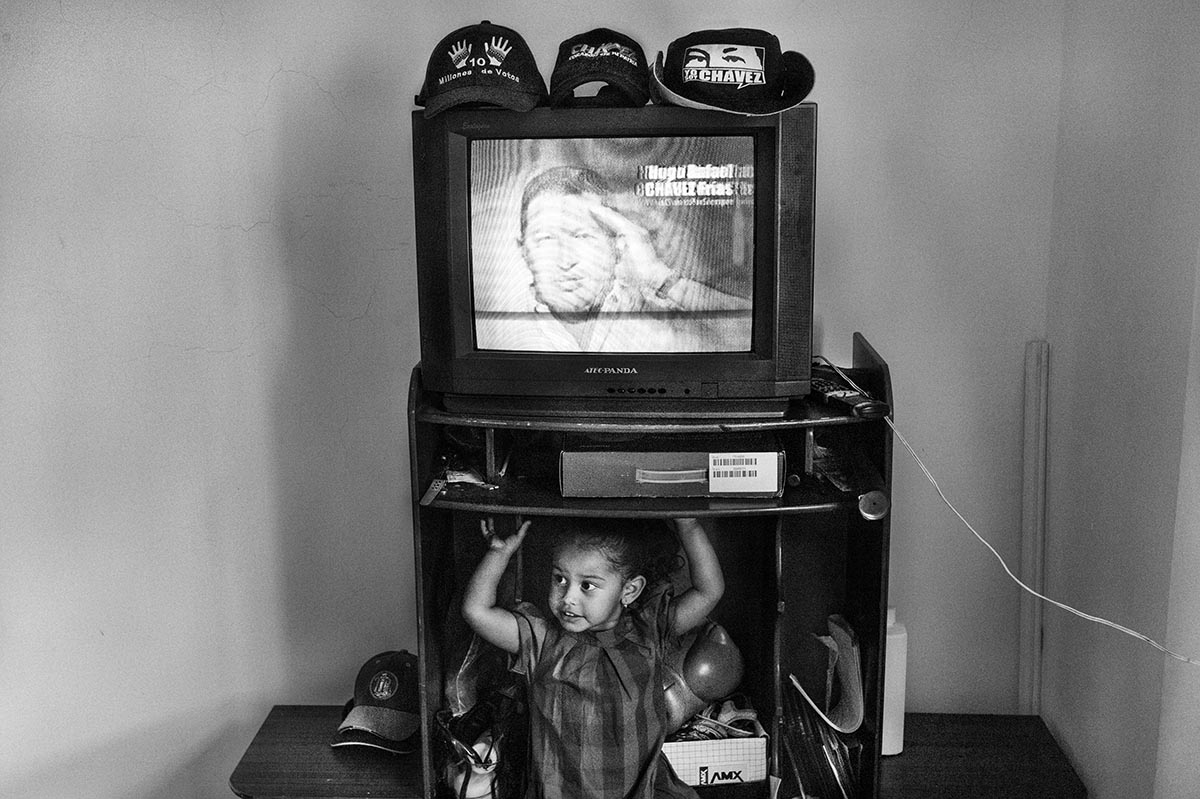 A child plays in a living room filled with images of Chávez in a government housing programme home