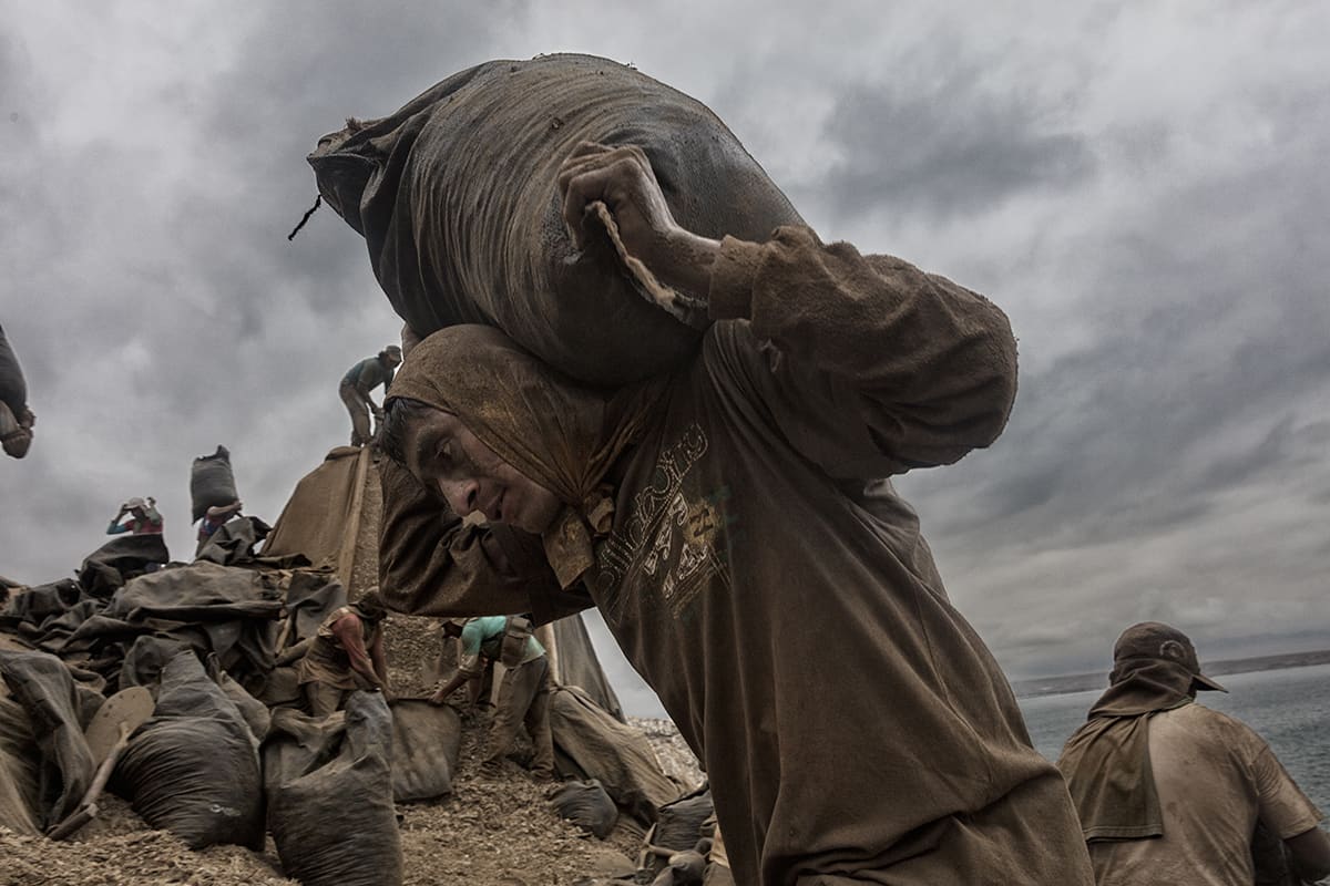 Guano worker carrying a 50-kilo sack of guano on his shoulders on Isla Asia, Peru.
