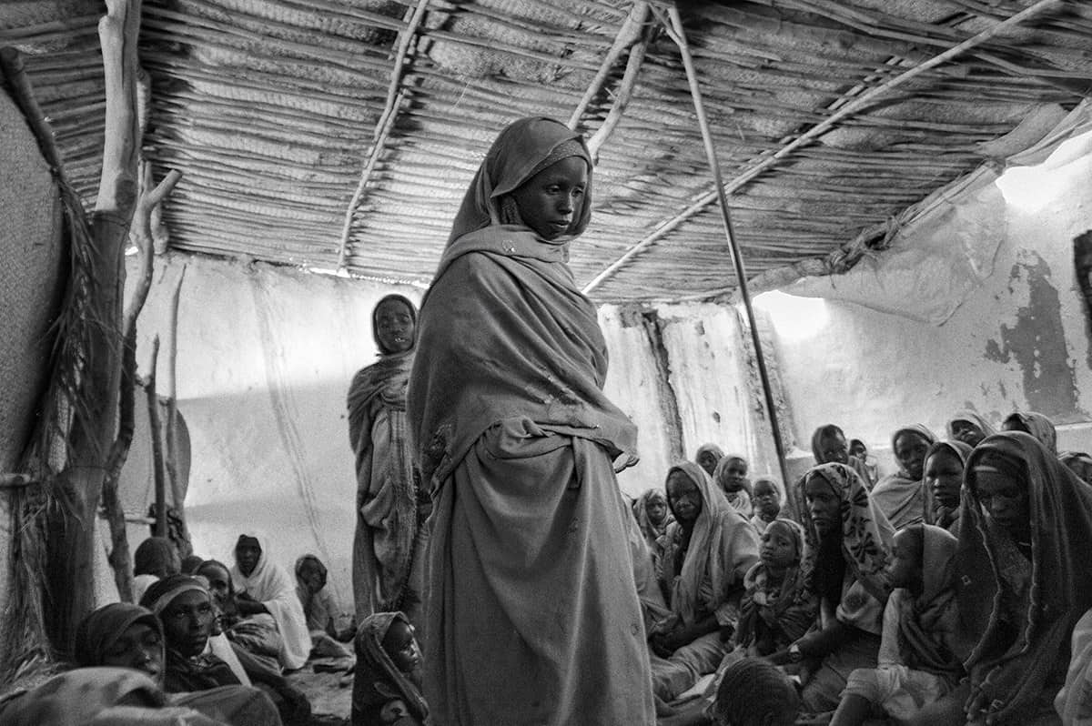 Displaced women and children gathered inside a straw shelter at a refugee camp in Darfur, Sudan.