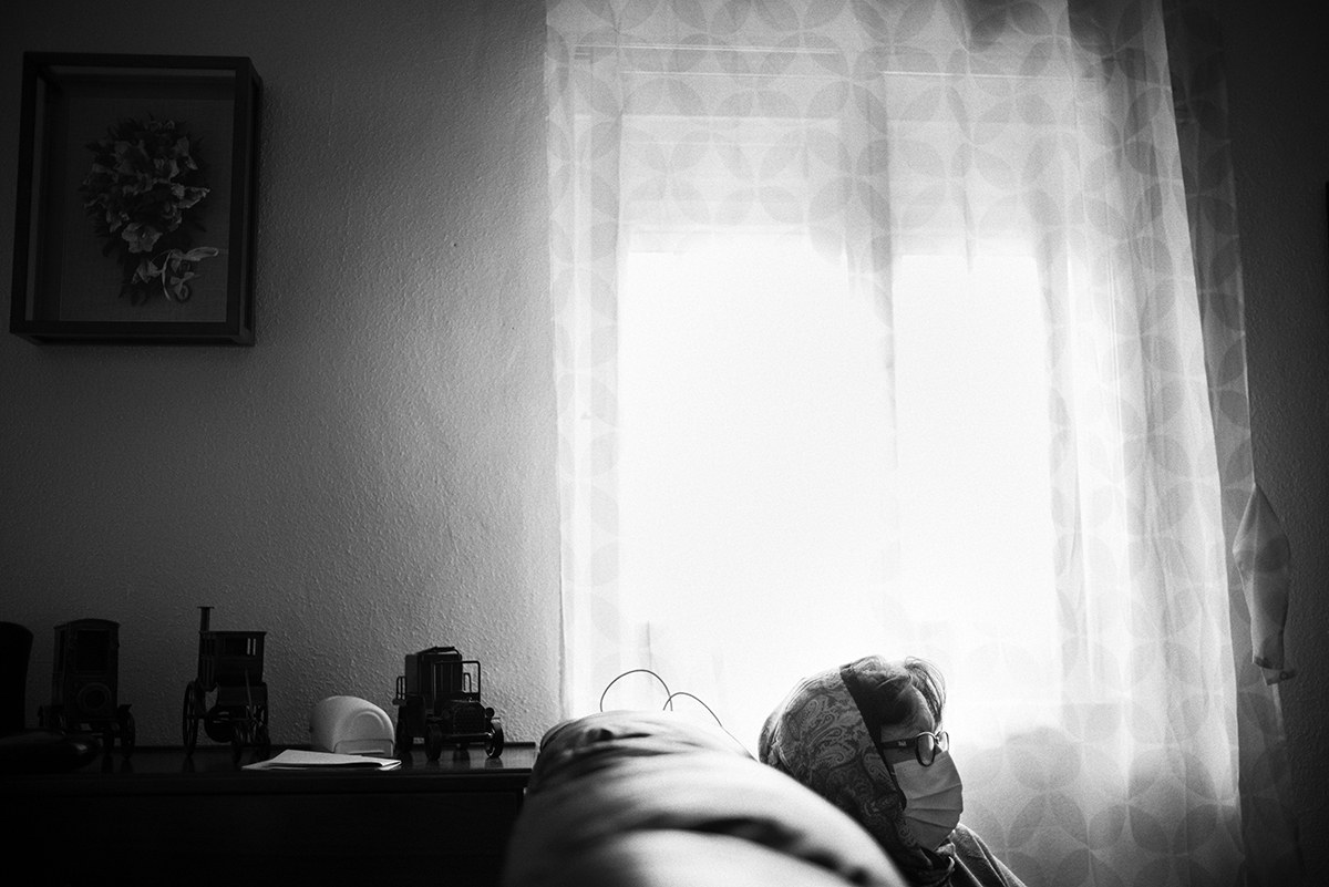 Elderly woman wearing a face mask sitting alone beside a window during the COVID-19 lockdown in Spain.