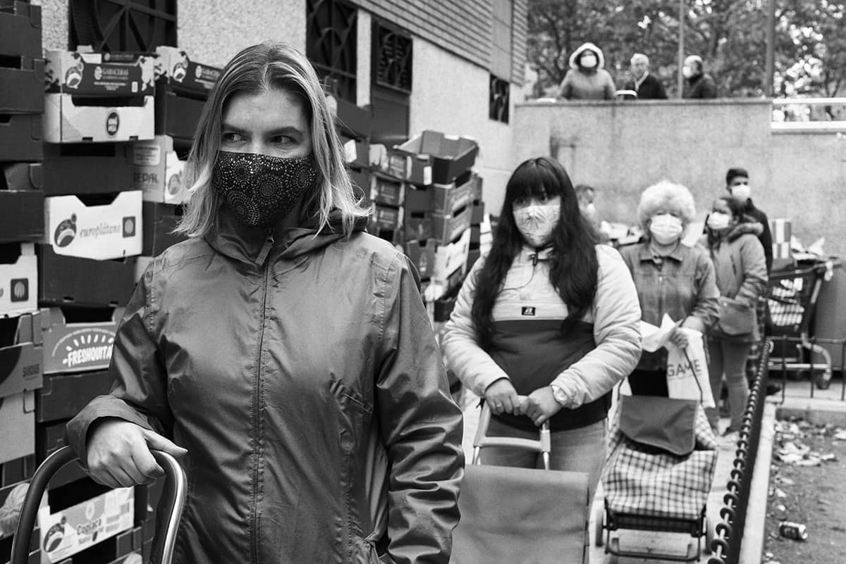 People wearing face masks queueing with shopping trolleys at a food bank distribution point in Spain during the COVID-19 crisis.