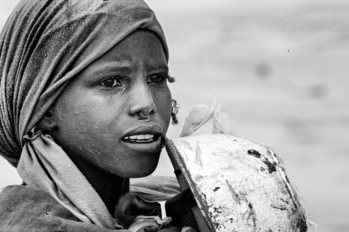 Girl carrying a metal water container on her shoulder at a displacement camp in Darfur, Sudan.