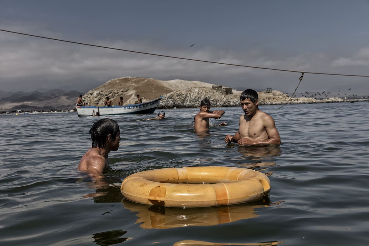 Guano workers bathing in the sea beside a boat after work on Isla Asia, Peru.