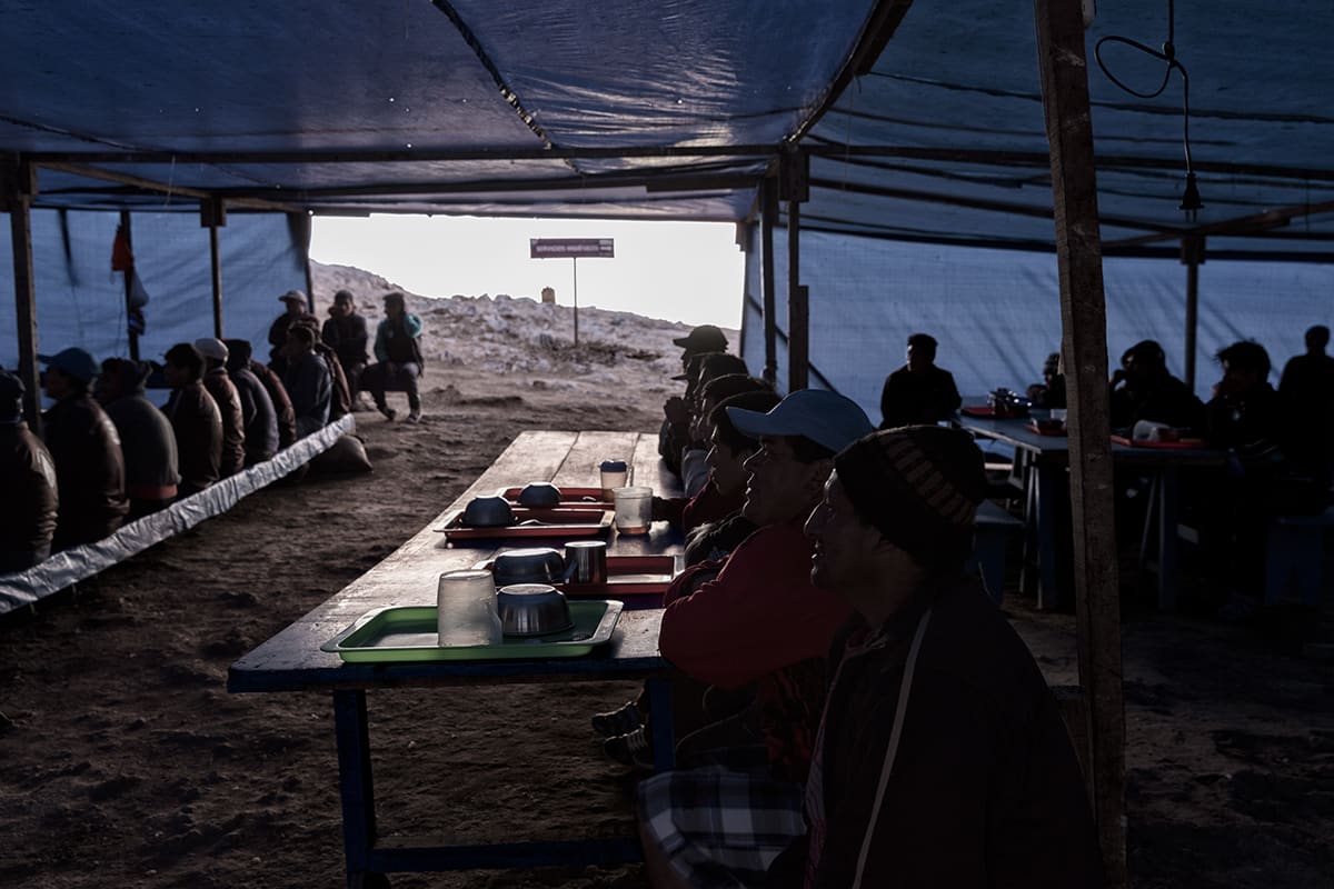 Guano workers having dinner at a long table under a tarpaulin on Isla Asia, Peru.