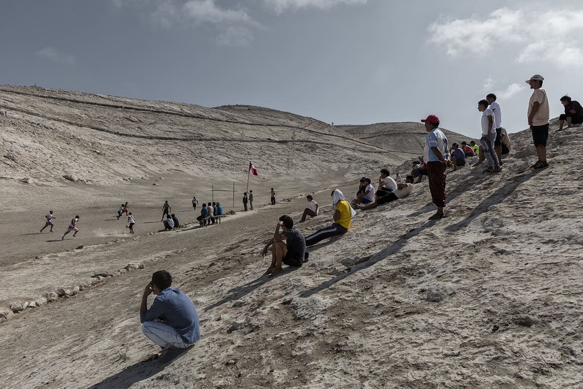 Guano workers playing a football match on a dirt pitch on Isla Asia, Peru.