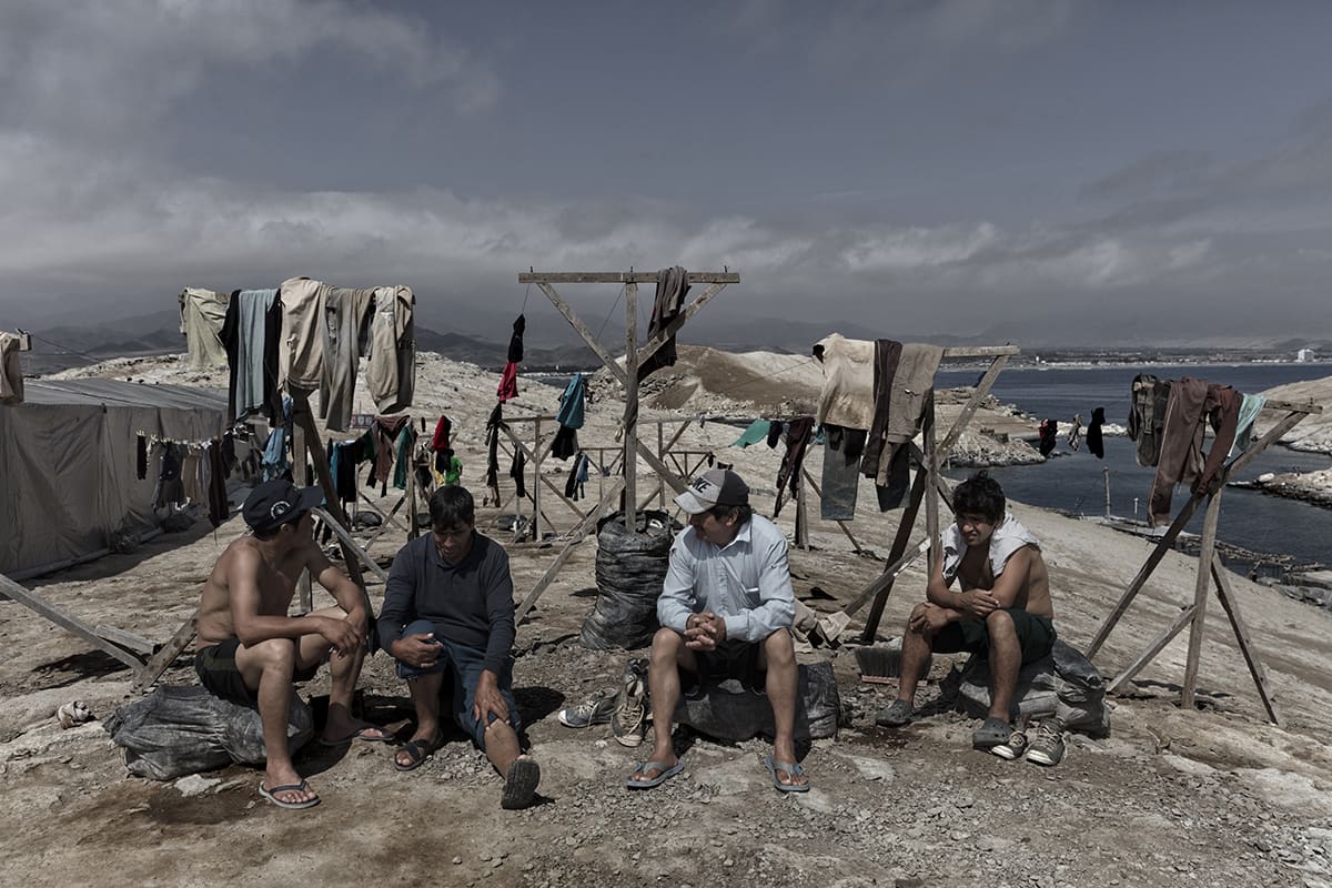Guano workers resting outdoors next to hanging laundry at the camp on Isla Asia, Peru.