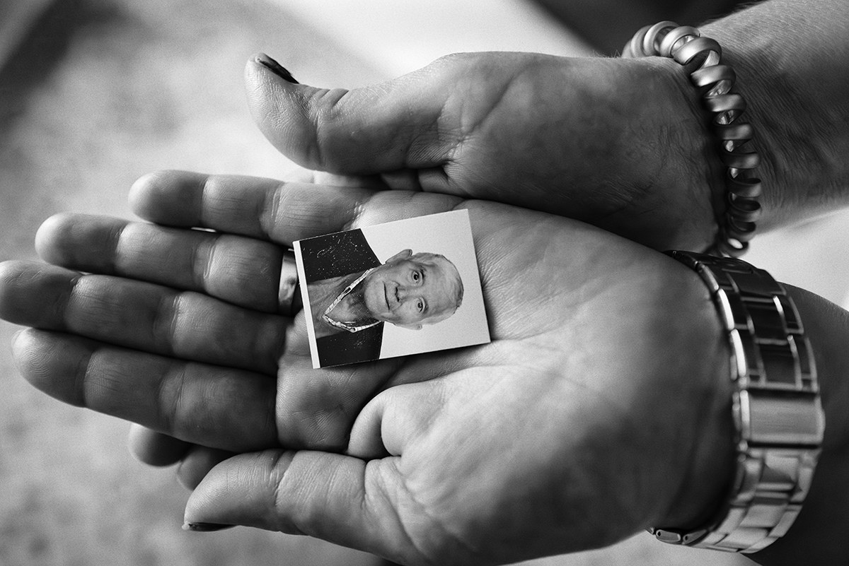 Hands holding a small portrait photograph of a relative who died of COVID-19 in Spain.