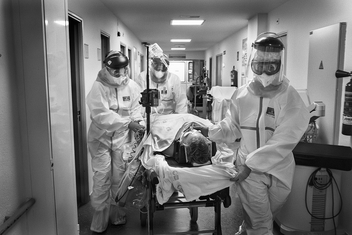 Healthcare workers moving a COVID-19 patient on a stretcher along a hospital corridor in Spain.