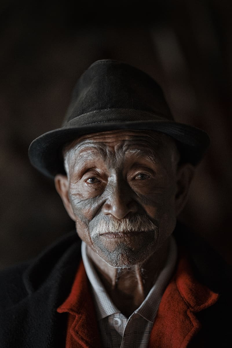 Konyak elder wearing a black hat, with a white moustache and tattooed face, Nagaland.