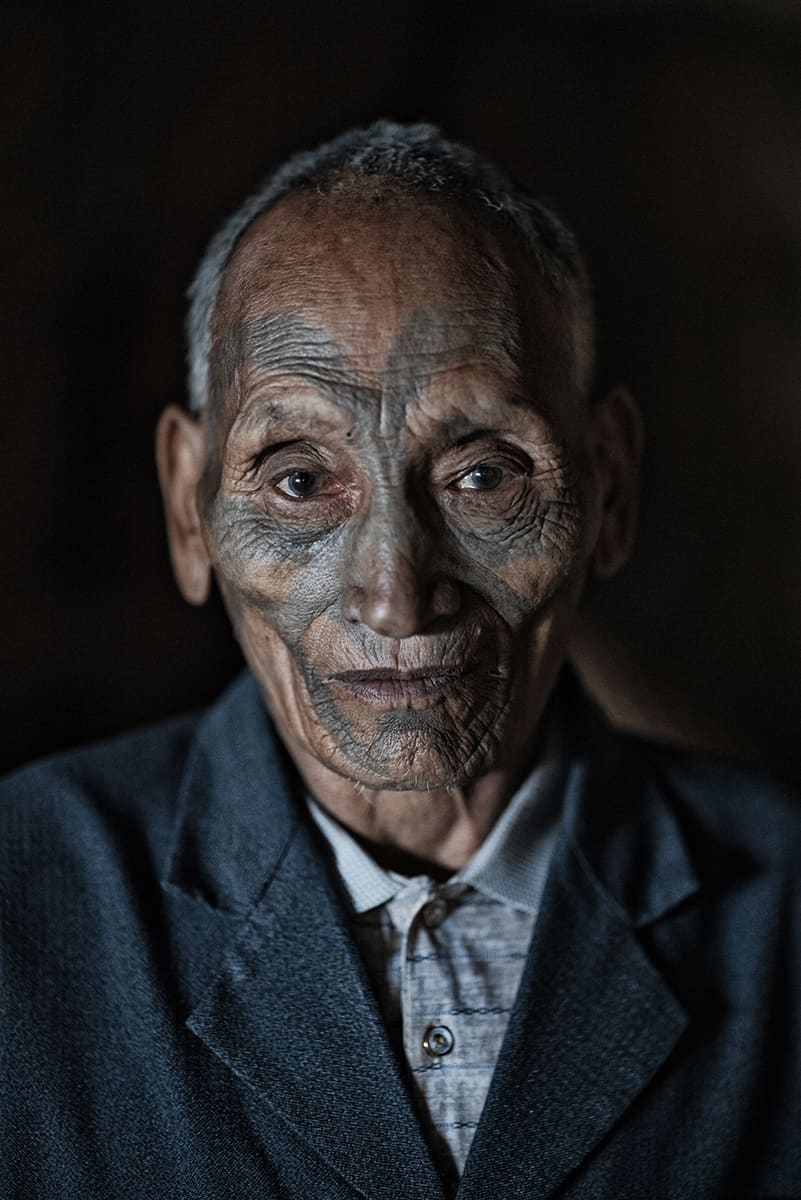 Portrait of a Konyak elder with facial tattoos wearing a jacket, Mon district, Nagaland.