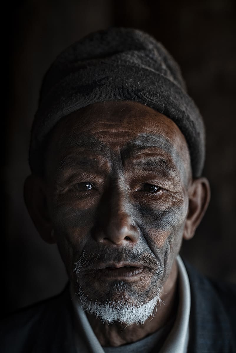 Konyak elder with a white beard and tattooed face, photographed inside his home in Nagaland.