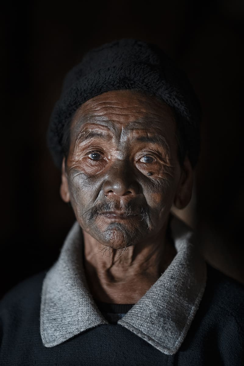 Konyak elder in a black wool cap, his face marked by traditional tattoos, Nagaland, India.