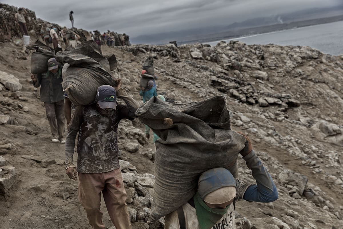 Line of guano workers carrying heavy sacks up a rocky path on Isla Asia, Peru.