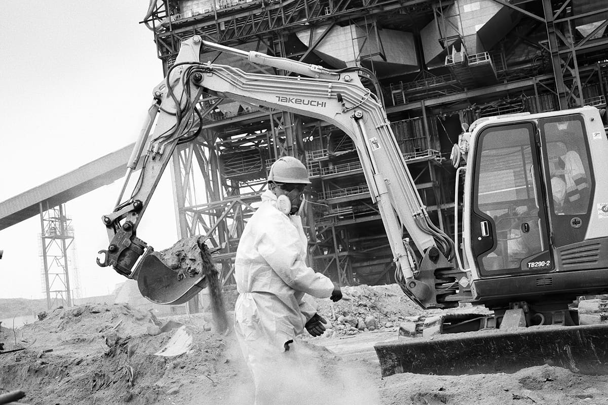 Worker in a protective suit and respirator beside an excavator during the dismantling of the Litoral thermal power plant, Carboneras, Almería, Spain, 2024