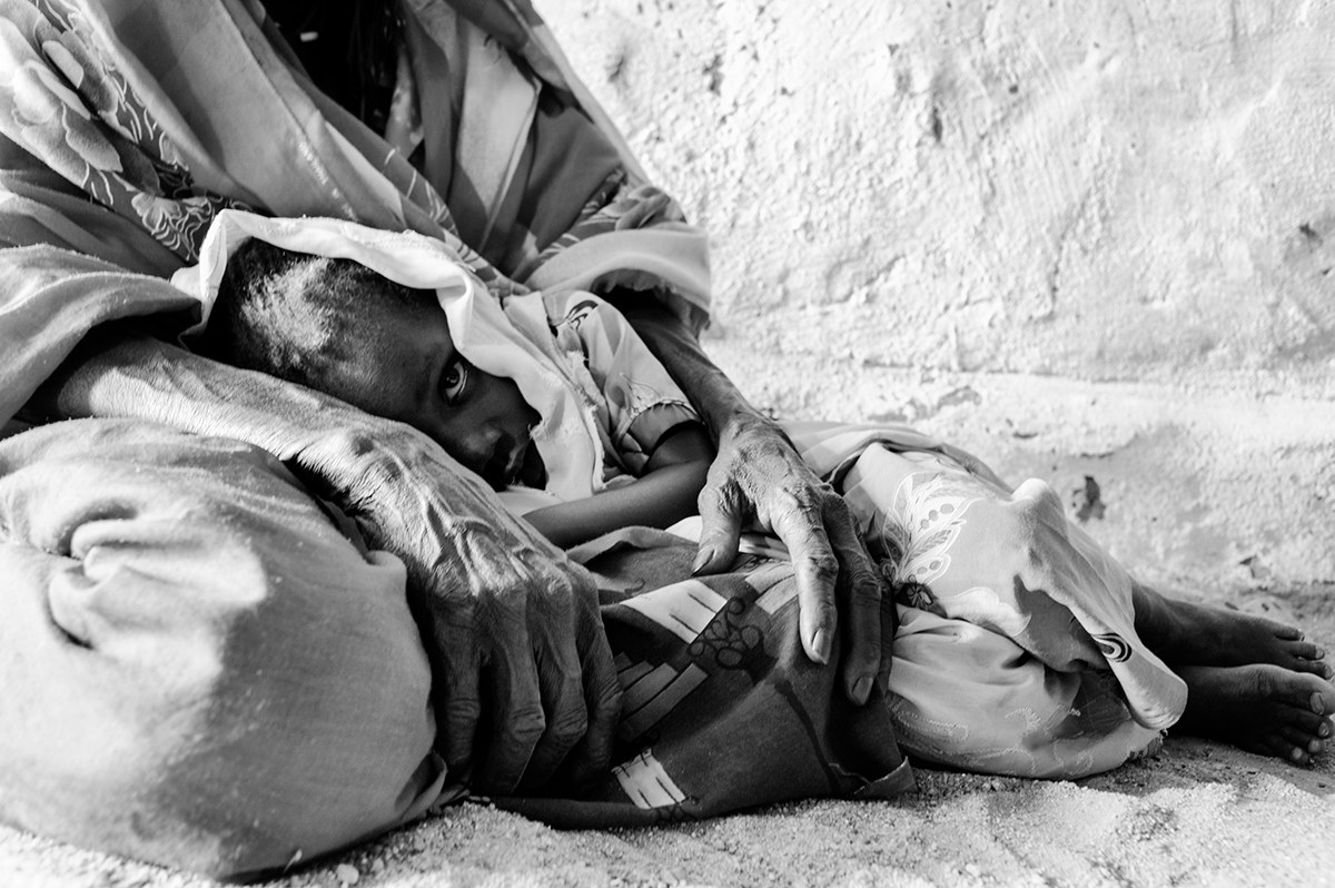 Mother holding her sick child on the ground beside a wall at a camp in Darfur, Sudan.