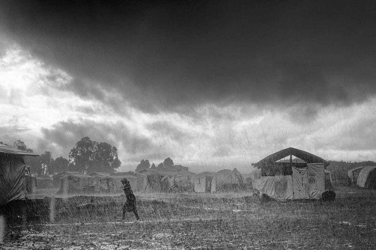 A refugee running for shelter through the rain in the Kibati refugee camp, North Kivu.