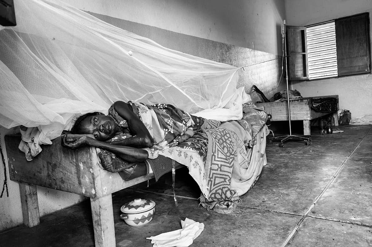 Sick woman lying under a mosquito net on a hospital bed in Darfur, Sudan.