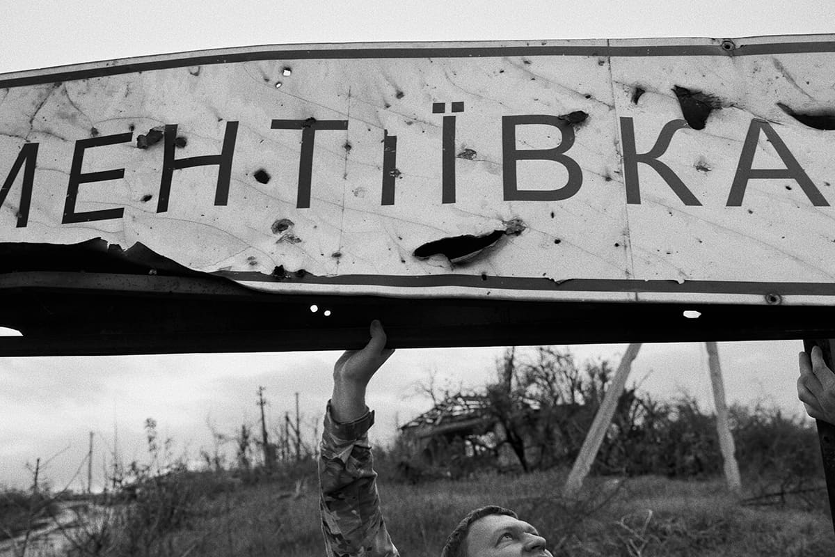A Ukrainian soldier raises the village sign of Dementiivka after the town was retaken.