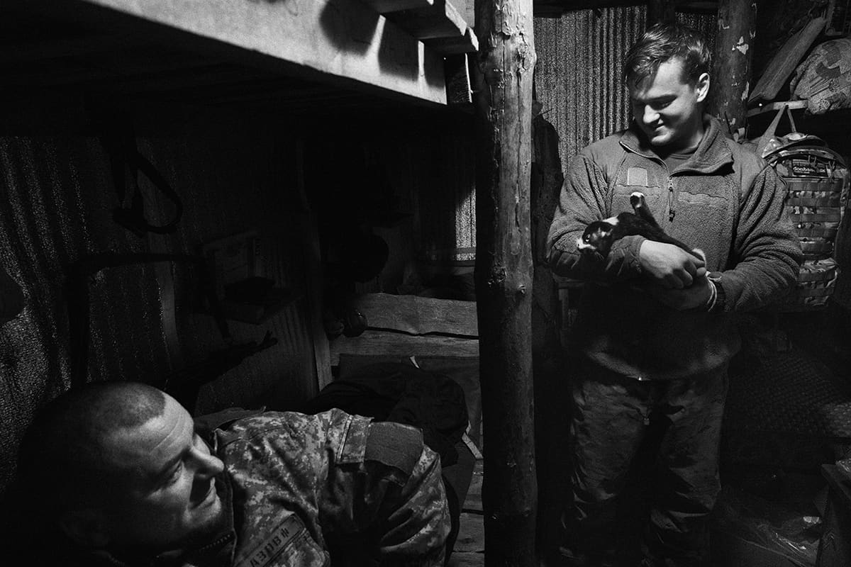 Vitaliy and Andriy talk in their trench on the Lyman front while one of them strokes their cat.