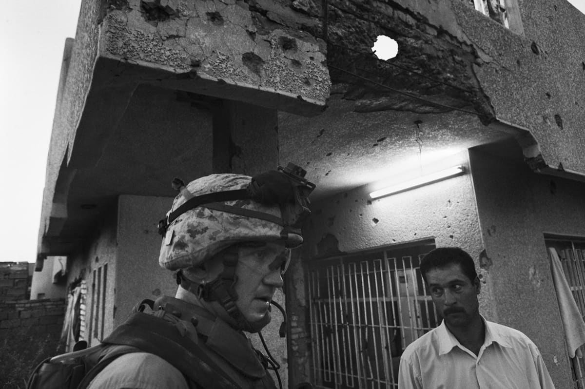 A US Marine from Bravo Company stands beside an Iraqi civilian in front of a bullet-riddled wall during a patrol in Fallujah