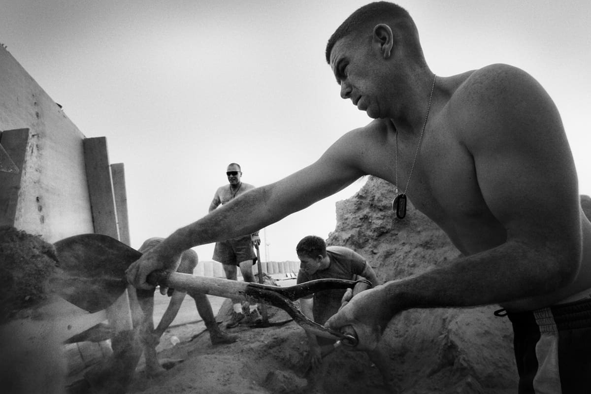 A shirtless US Marine shovels sand to fill sandbags during the Ramadi insurgency Iraq
