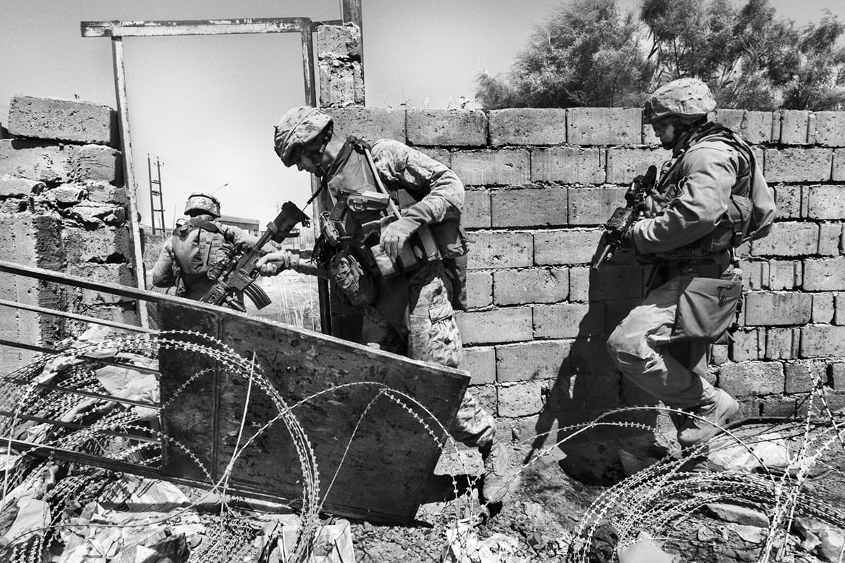 US Marines from Bravo Company crossing rubble inside a damaged building during a Fallujah patrol — an image of the urban warfare reality of the Iraq War 2003