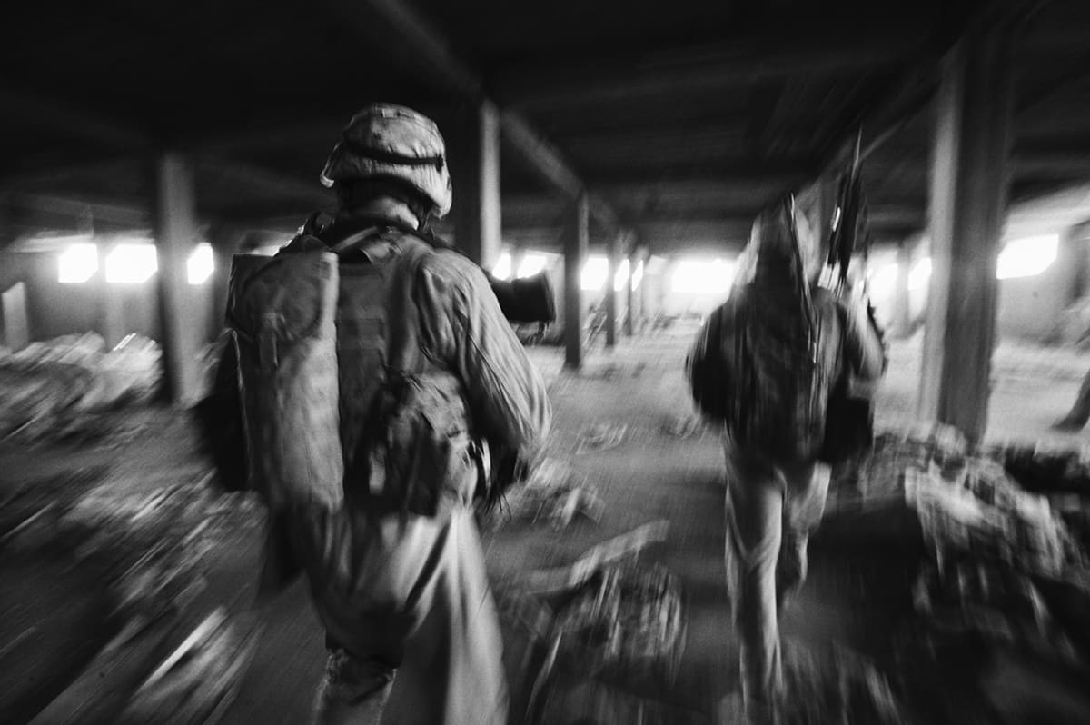 Blurred figures of US Marines from Bravo Company running through an abandoned building in Fallujah after taking sniper fire — the urban warfare reality of the Fallujah battle Iraq
