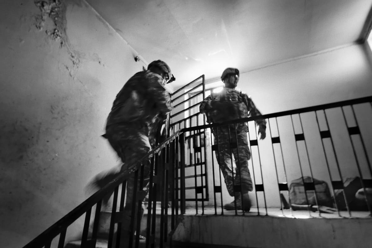 US QRF soldiers ascending a darkened staircase with flashlights during a joint raid with Iraqi police in Baghdad — a daily scene of insurgency and occupation