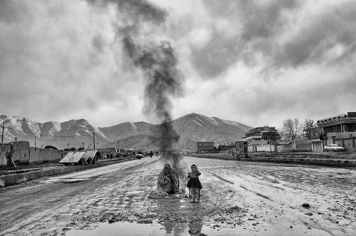 Woman in burqa and child warming themselves by a fire in the middle of a muddy road in Kabul, February 2009