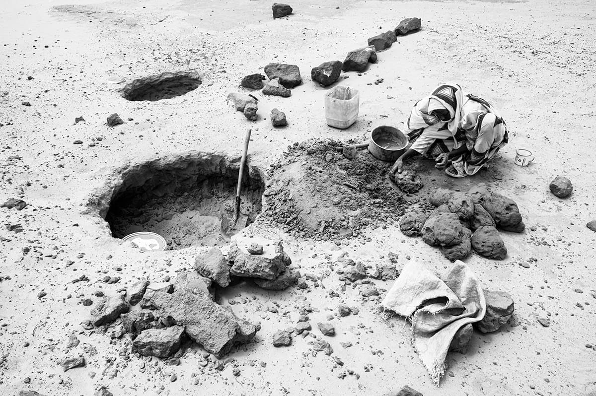 Woman digging a water hole in a dry riverbed to reach groundwater in Darfur, Sudan.