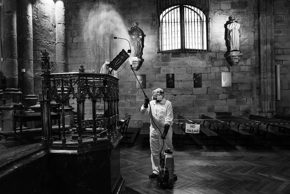 Worker in a protective suit disinfecting the interior of a church with a No Pasar sign during the COVID-19 pandemic in Spain.